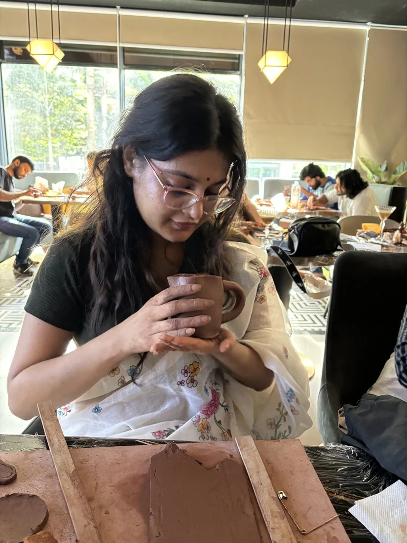 A person wearing glasses examining a hand shaped clay cup at a pottery table