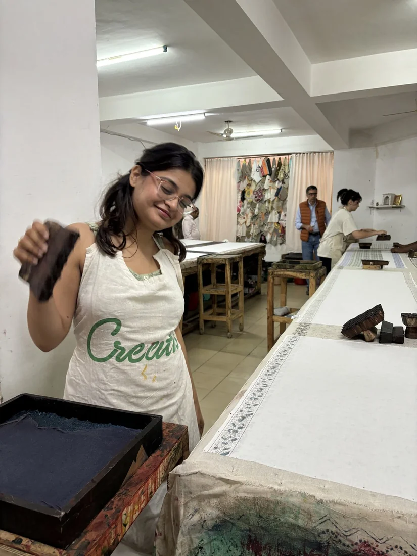 A person in a printing apron lifting a wooden block over an ink tray in a block printing studio